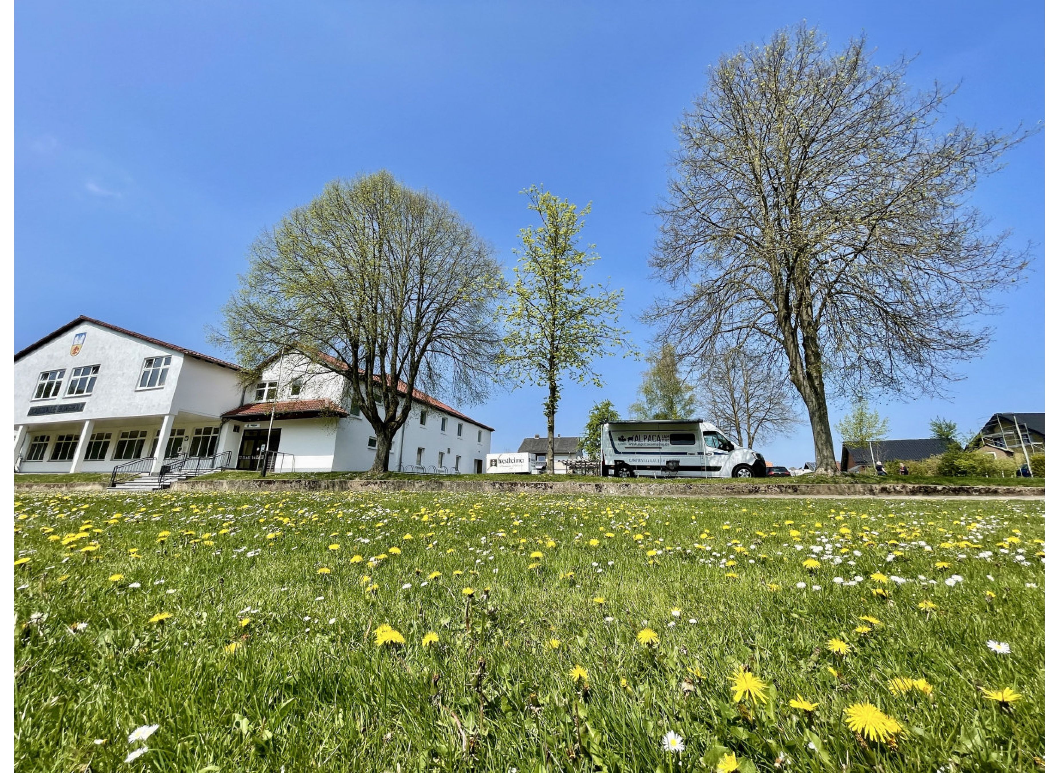 Stellplatz auf einem Hallenvorplatz neben einer grünen Wiese